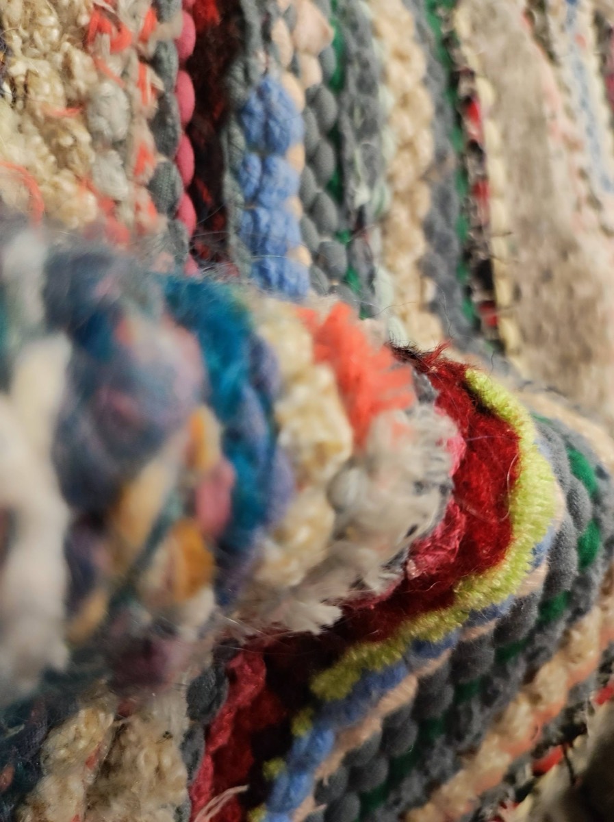 Close-up of a rug woven from strips of old clothes in red, lime, blue, coral and cream